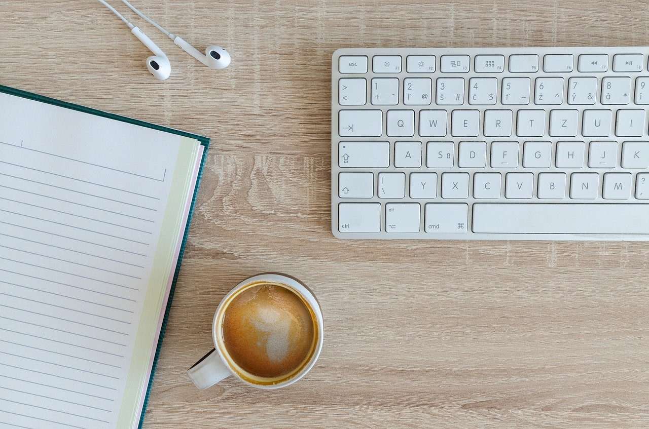 Desk top with book, coffee, laptop keyboard and headphones